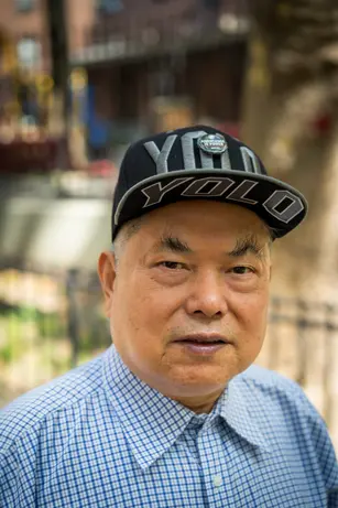 An older man in a checked shirt and a YOLO snapback with a "Knowledge is Power" pin looks directly at the camera, a city street soft behind him.