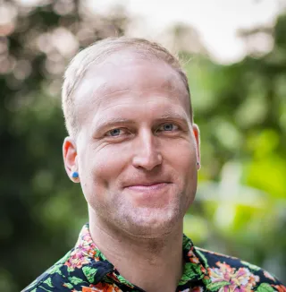 Jaan Altosaar, smiling in a floral shirt against blurred greenery.