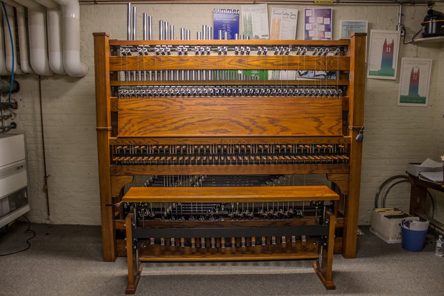 The carillon's wooden playing console: two rows of dowel levers and a pedalboard, with steel rods running up out of frame to the bells.