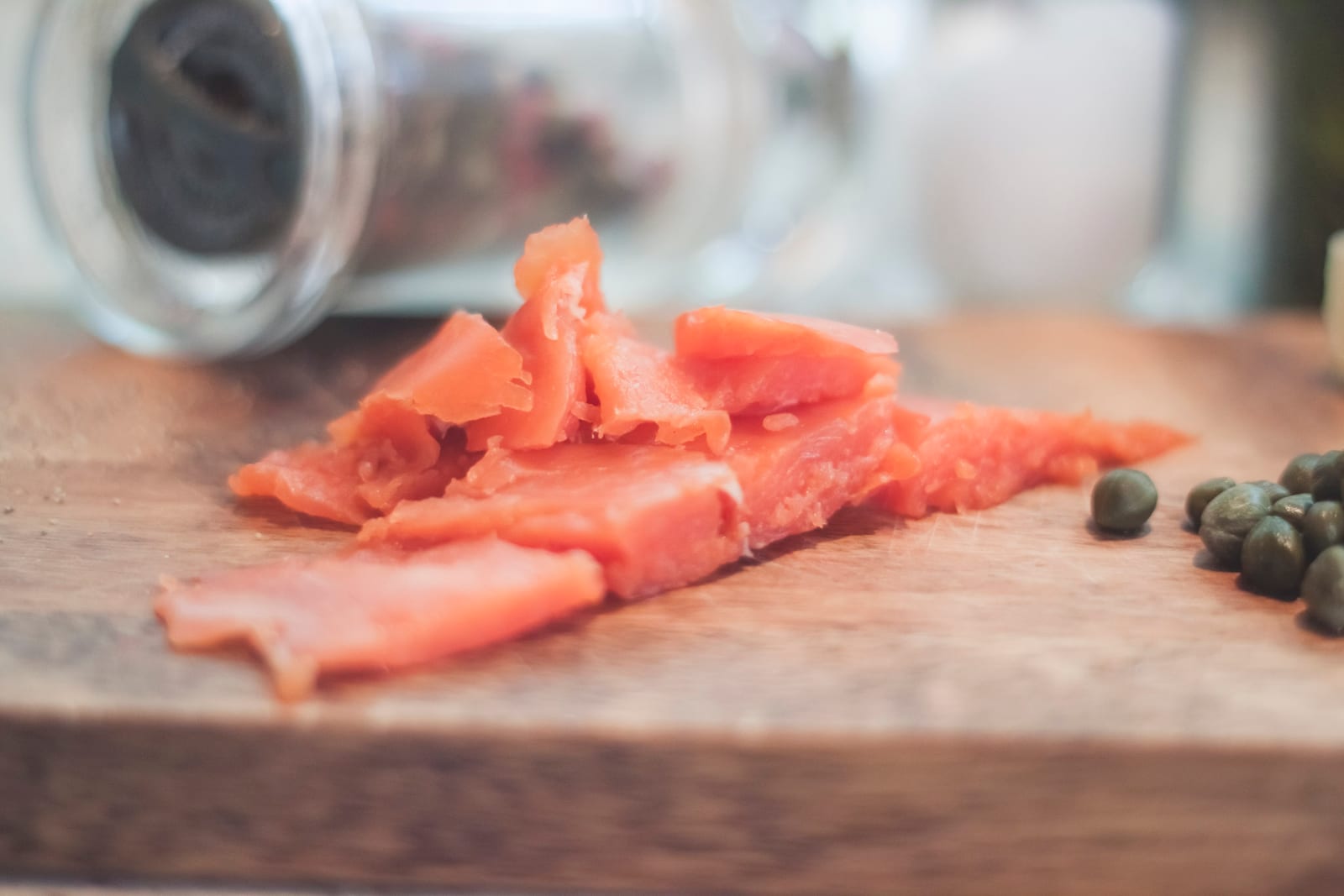 A heap of hand-sliced smoked salmon on a wooden cutting board, a scattering of capers beside it.