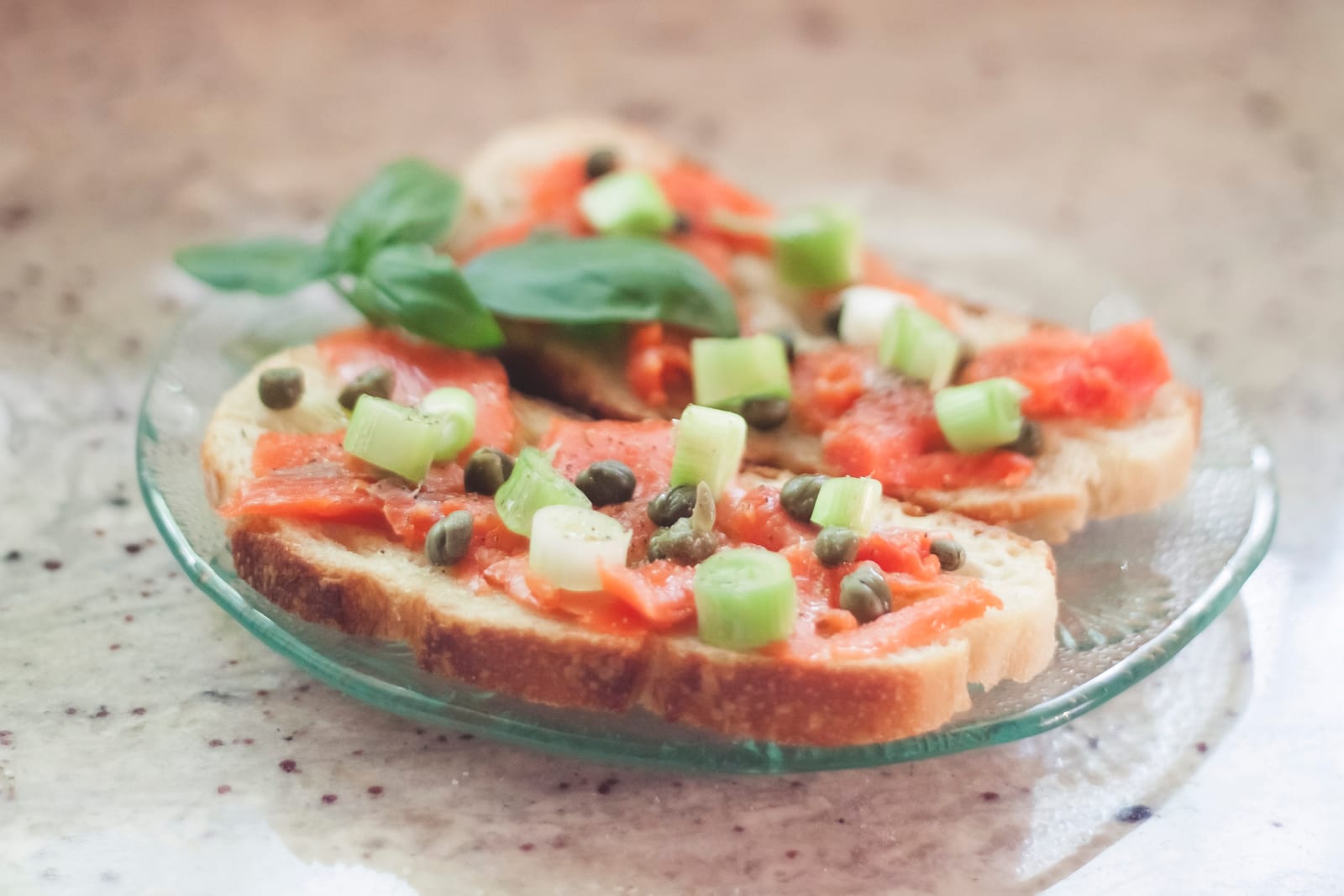 The finished sandwiches on a glass plate, salmon covered in diced green onion, capers and a few basil leaves.