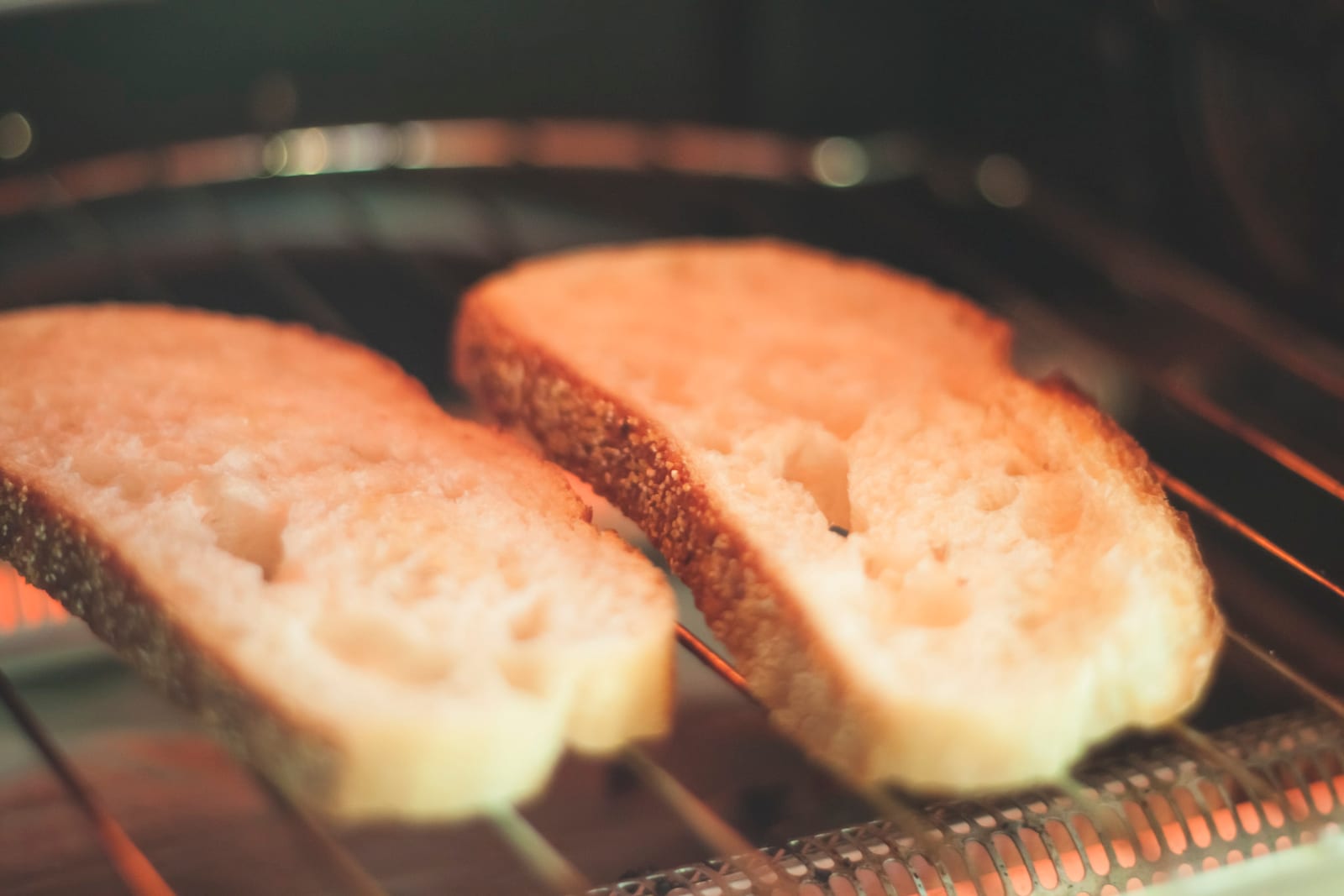 Two thick slices of white bread toasting on an oven rack, the edges going gold.